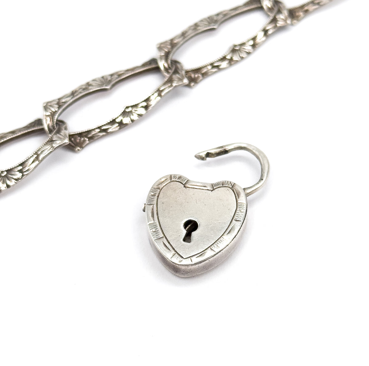 Close view of the heart lock from above, its banded rim and keyhole sharp and the rounded side showing its thickness, while the floral links trail off diagonally out of the upper corner.
