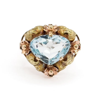 Close overhead crop on the face, filling the frame so the aquamarine's broad triangular facets and the four rose gold flowers between green gold leaves read in fine detail.