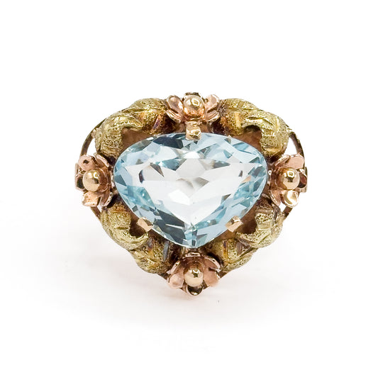 Close overhead crop on the face, filling the frame so the aquamarine's broad triangular facets and the four rose gold flowers between green gold leaves read in fine detail.