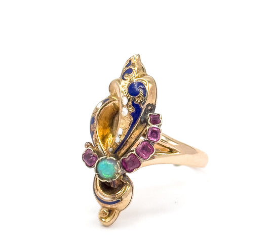 Upright view from the front edge, showing rows of tiny white enamel dots trailing along the blue enamel scrolls, the opal set low on the face and the shank curving away to the right.
