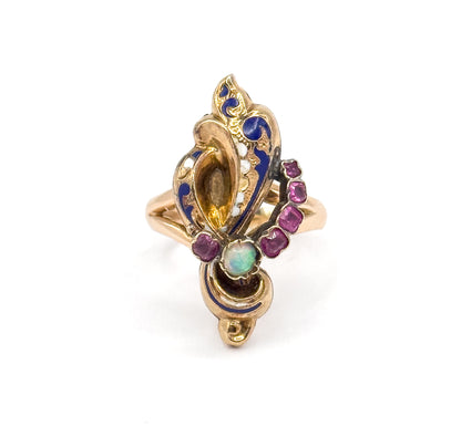 Straight-on view of the whole face, the cobalt blue and white enamel scrolls forming a tapering freeform outline, with the opal centred low and the five rubies stepping up its right side.