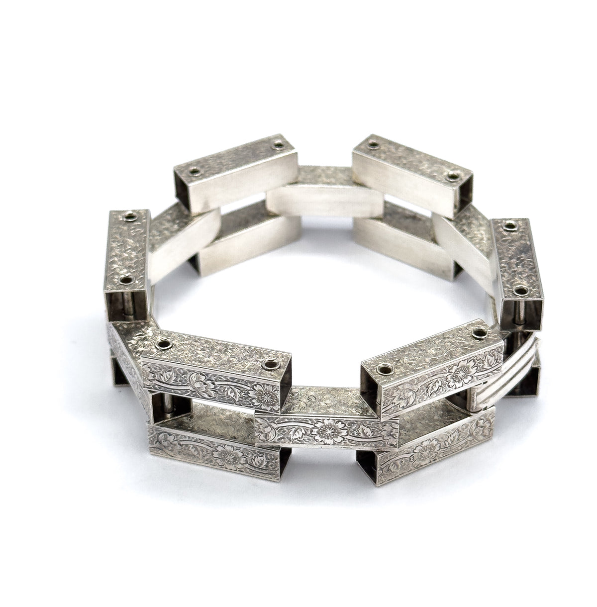 A low, near eye-level view across the standing ring, where the front links show their floral engraving while the far links are seen from inside as plain, smooth bars.