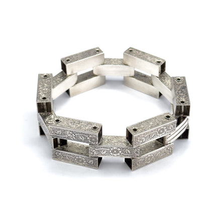 A low, near eye-level view across the standing ring, where the front links show their floral engraving while the far links are seen from inside as plain, smooth bars.