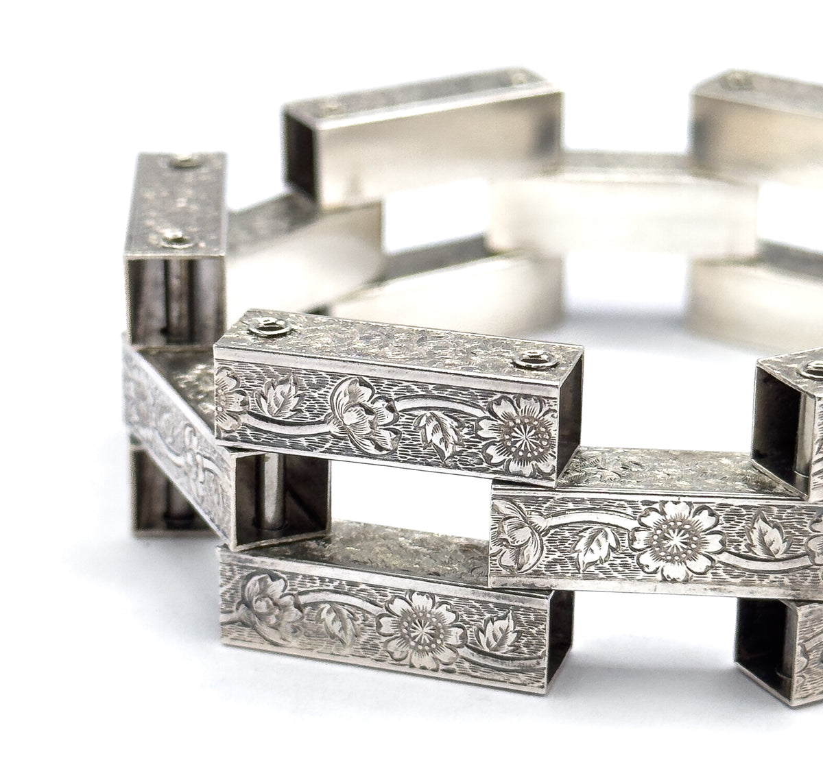 Close macro on two foreground bars, where the repeating engraved flowers, buds and leaves fill the surface and the hinge pin heads sit at each end of the link.