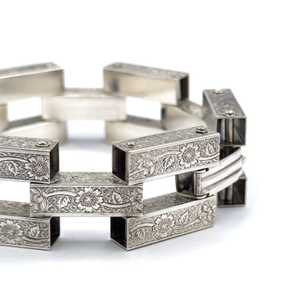 Sharp close-up on the clasp end, where a hinged bar folds in against the engraved gate links and a small pin holds the closure between the square openings.