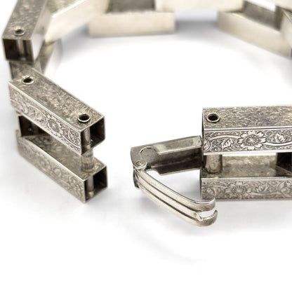 Open-clasp view with the two ends apart, the hollow square link interiors visible on the left while the ribbed fold-over catch hangs swung open from the engraved end on the right.