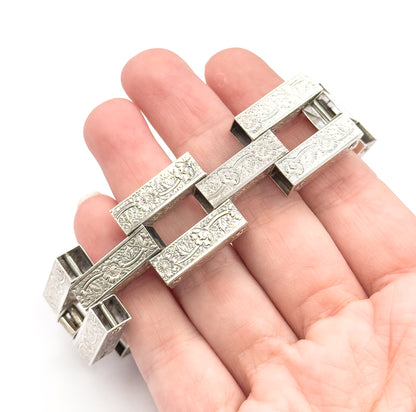 The bracelet rests across an open palm, giving a sense of scale: the broad floral-engraved bars span nearly the full width of four fingers.