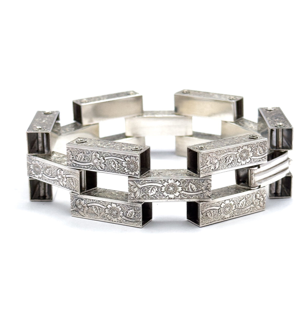 The bracelet stands upright in a full circle on a white background, its sterling silver gate links forming an open ring of floral-engraved bars with square gaps between them.