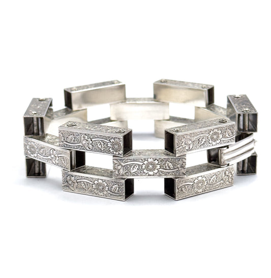 The bracelet stands upright in a full circle on a white background, its sterling silver gate links forming an open ring of floral-engraved bars with square gaps between them.