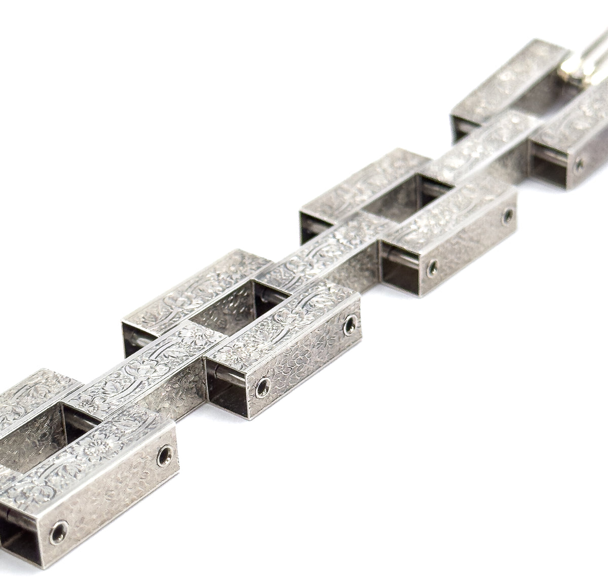 A sterling silver gate link bracelet, shown laid out diagonally on a white background, its chunky hinged links engraved with repeating floral patterning along each broad bar.
