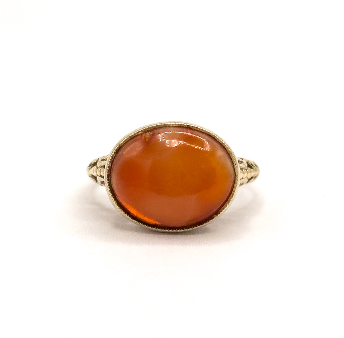 Upright front view with the ring standing on its shank, the oval coral cabochon glowing orange in its milgrain bezel and the filigree shoulders seen almost edge-on to either side.