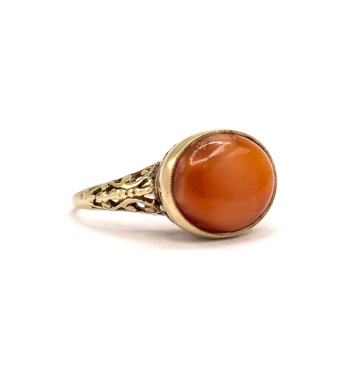 Side profile against white, showing the oval coral cabochon standing proud in its milgrain bezel above openwork filigree shoulders that taper into the slim shank.