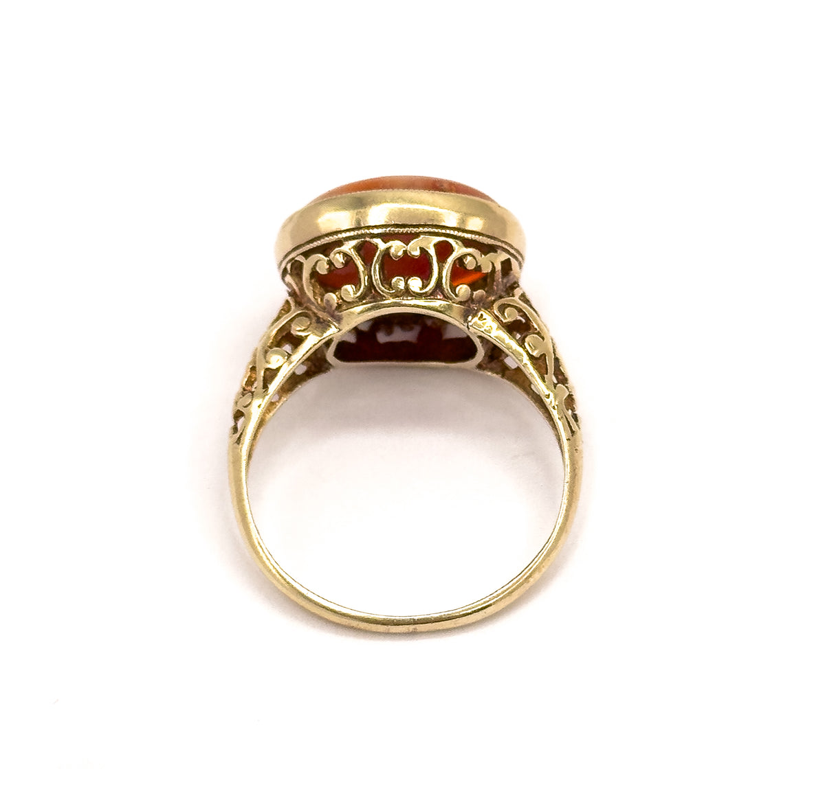 Viewed end-on through the open circle of the shank, looking up at the scrolled filigree gallery beneath the bezel with the coral just visible above.
