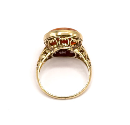 Viewed end-on through the open circle of the shank, looking up at the scrolled filigree gallery beneath the bezel with the coral just visible above.