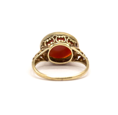 Rear view from behind the shank, looking into the open back of the setting where the coral shows through the aperture, framed by scrolled filigree and the slim band curving below.
