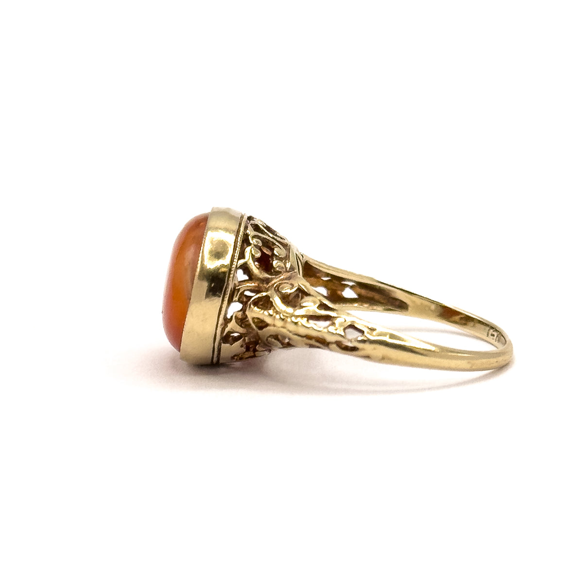 Opposite side profile on white, the coral cabochon seen from its other edge with the milgrain bezel rim catching light and filigree scrolls arching down the shoulder into the shank.