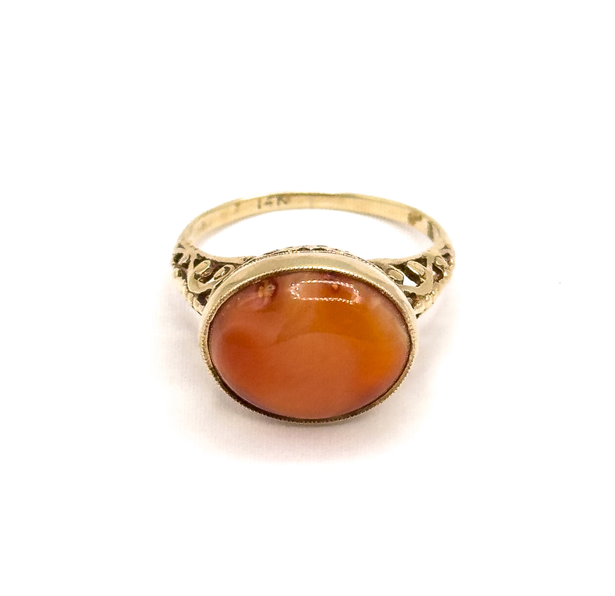 Face-on from above, the oval coral cabochon filling its milgrain bezel with pierced filigree shoulders flaring symmetrically to either side and the slim shank arching behind.
