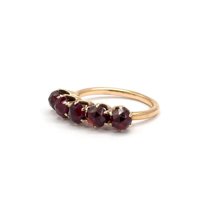 Raised three-quarter view with the ring balanced upright, the five rose cut garnets angled across the frame so their faceted domes catch the light within the clawed yellow gold prongs.