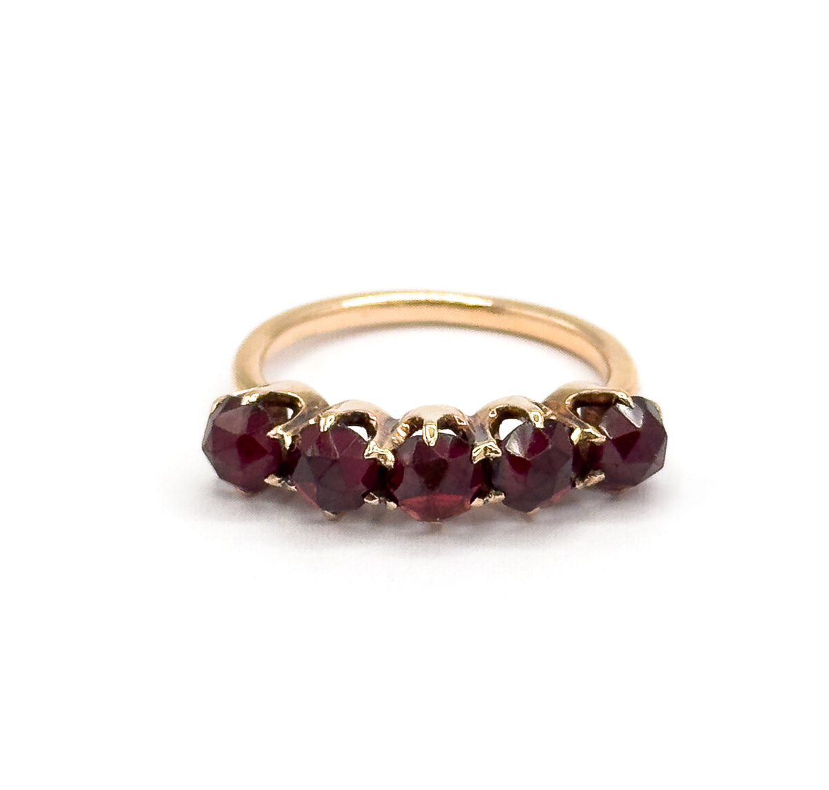 Straight-on front view of the five rose cut garnets in a level row, each held by yellow gold claw prongs, with the plain round shank rising in a loop behind them.