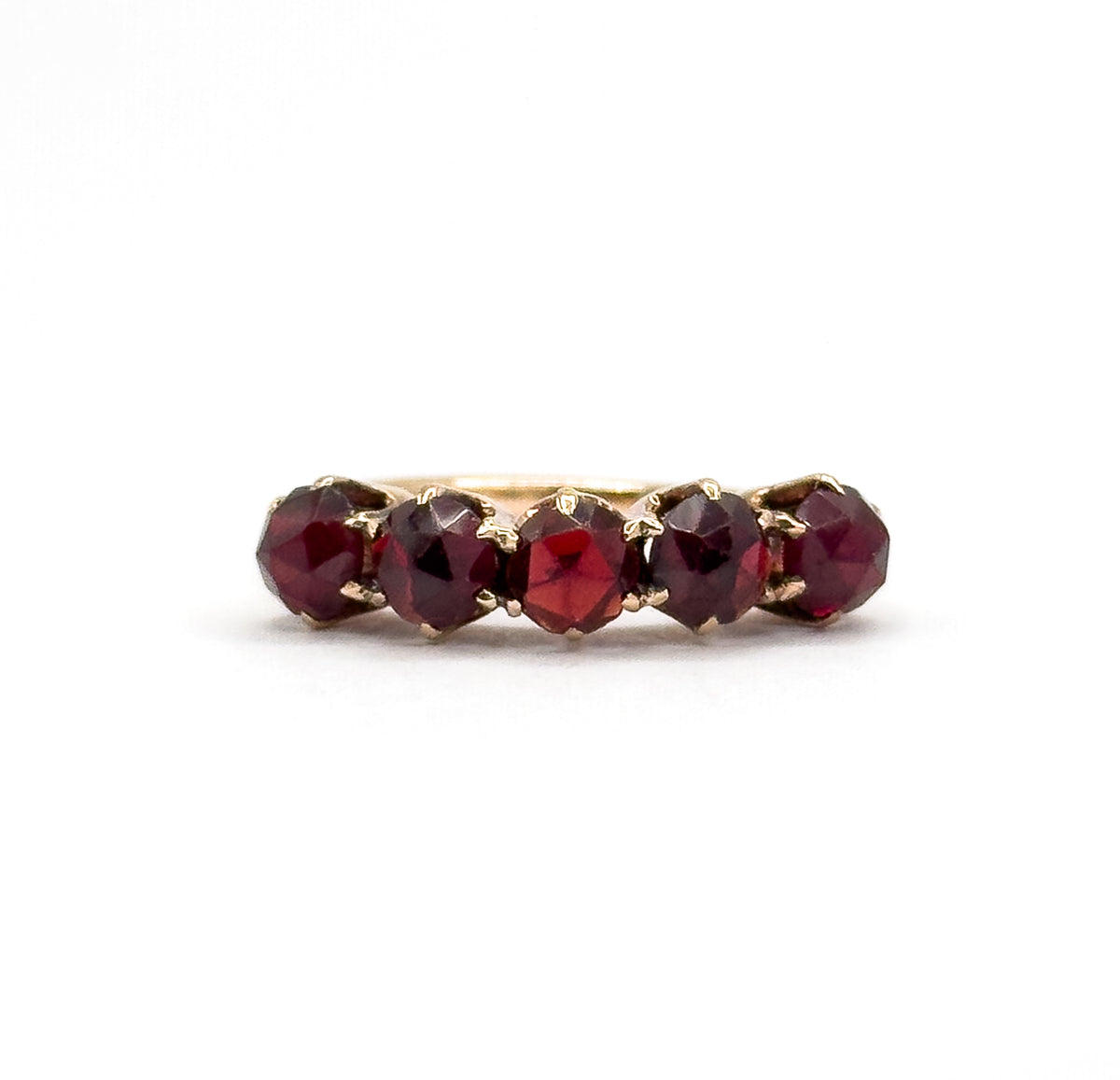 Tight close crop on the row from just above, the five deep red rose cut garnets filling the frame with their claw prong tips catching light and only a sliver of the yellow gold shank behind.