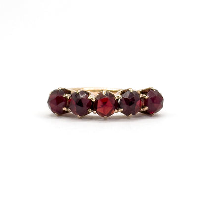Tight close crop on the row from just above, the five deep red rose cut garnets filling the frame with their claw prong tips catching light and only a sliver of the yellow gold shank behind.