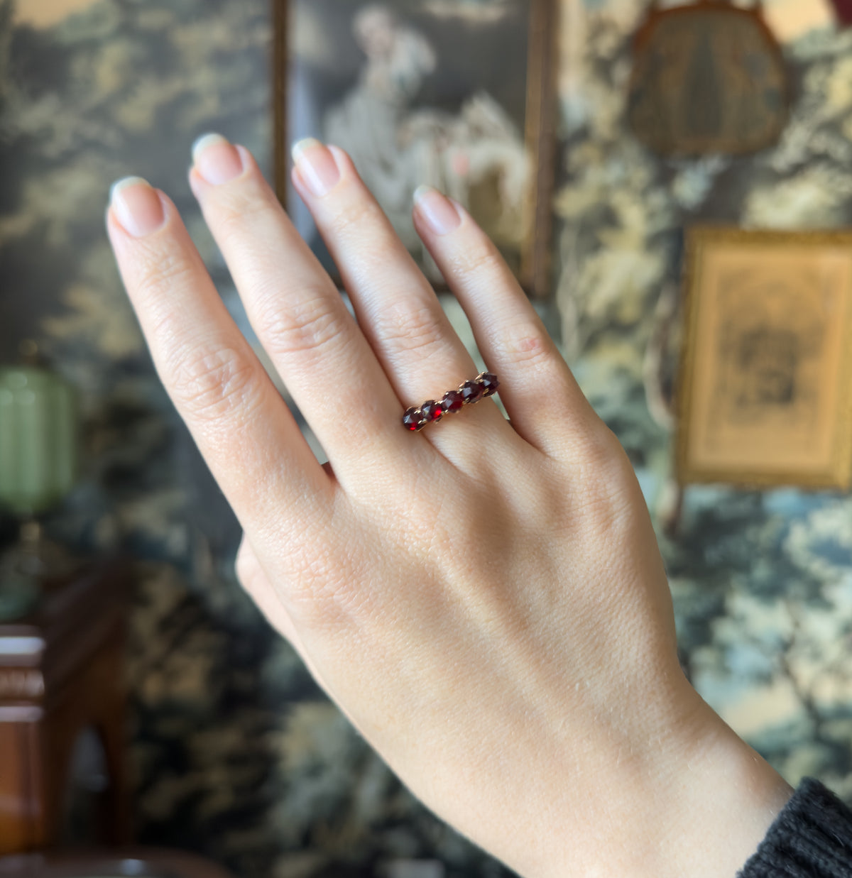Shown on the ring finger of a raised hand, the five deep red stones reading as a small row across the face, which gives a sense of the ring's modest scale.