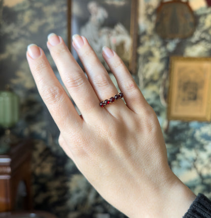 Shown on the ring finger of a raised hand, the five deep red stones reading as a small row across the face, which gives a sense of the ring's modest scale.