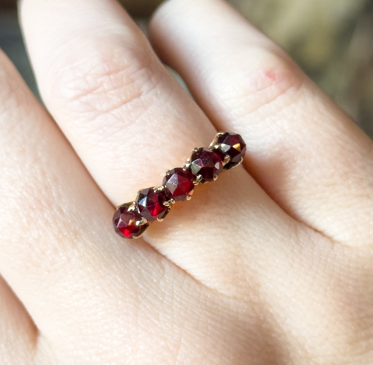 Looking down the row from one end, the five rose cut garnets line up in receding perspective against the finger, each dome's facets glinting between the small gold prongs.