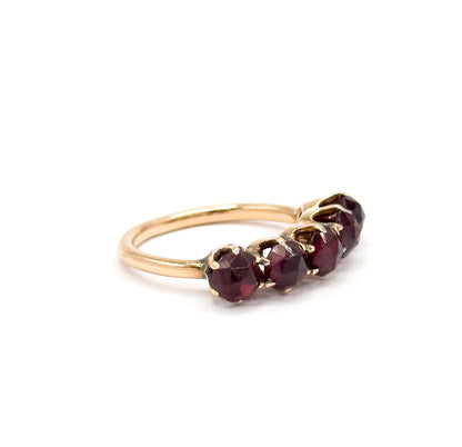 Off the hand against a plain white background, the ring stands on its slim yellow gold shank with the five deep red garnets angled toward the viewer in their prongs.