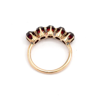 Viewed from behind, the open pierced gallery beneath the five garnets is visible between the prongs, with the slim yellow gold shank forming a full circle below.