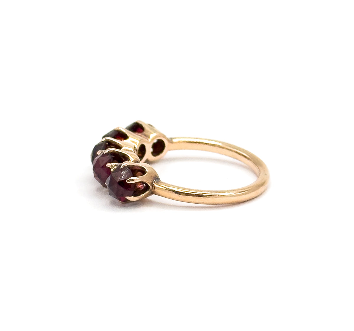 Side-on close view with the row foreshortened, showing how low the prong-set garnets sit above the finger and how the slim yellow gold shank sweeps away behind them.