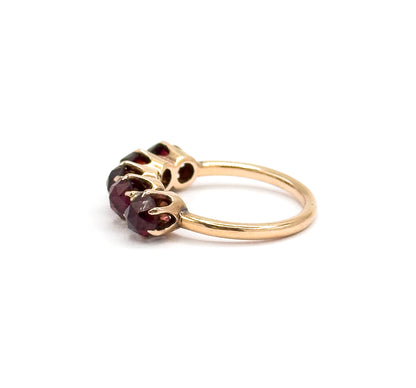Side-on close view with the row foreshortened, showing how low the prong-set garnets sit above the finger and how the slim yellow gold shank sweeps away behind them.