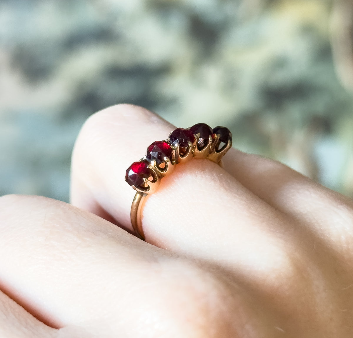 Vintage five stone rose cut garnet ring in 14K yellow gold, shown on a finger in close side view, the deep red stones held in prongs along the slim shank.