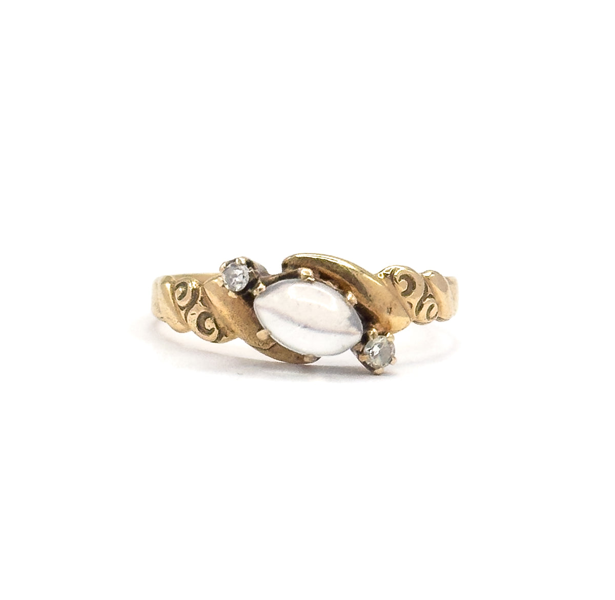 Upright front view with the ring filling the frame, the moonstone cabochon lying crosswise between its prongs and a diamond set above left and below right along the swirled gold shoulders.
