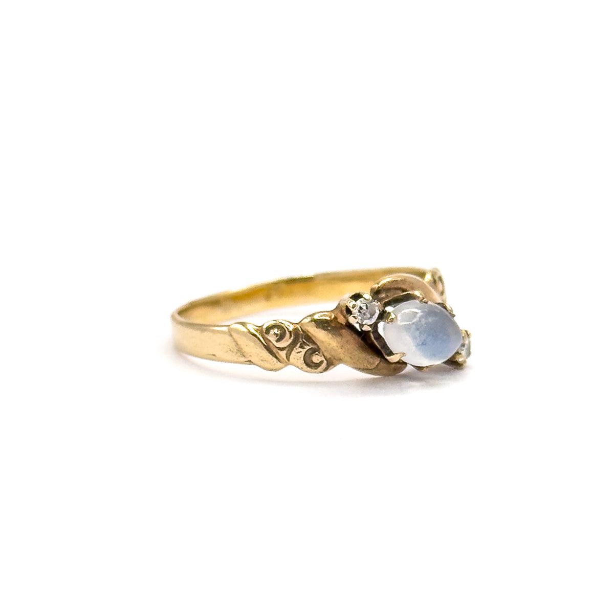 Side profile against plain white, off the hand, showing the low prong-set cabochon and one diamond at the face with the swirl design engraved into the tapering shoulder.