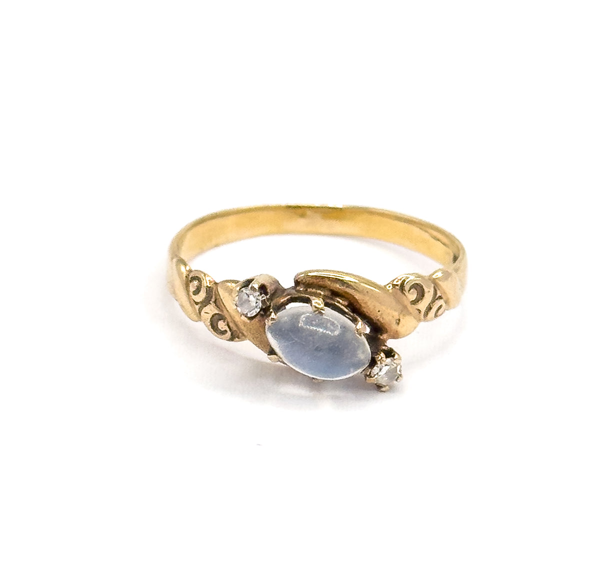 Three-quarter front view of the ring standing upright on white, the moonstone cabochon and both prong-set diamonds reading diagonally across the face between the swirled yellow gold shoulders.