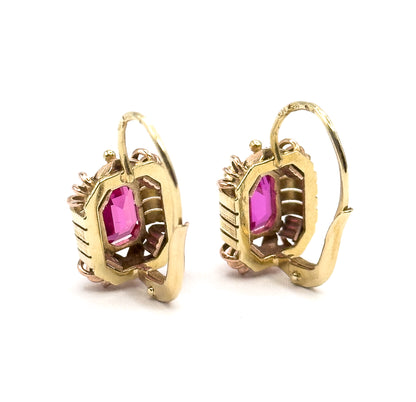 Both earrings seen from the side and slightly behind, showing the open gallery backs of the bezels, the ribbed frame edges and the long curved hook wires swinging out behind.