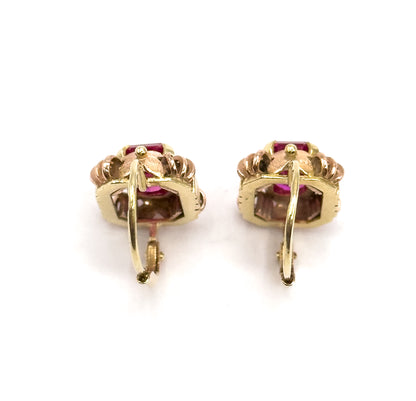 Rear view of the pair standing upright side by side, the hinged hook fittings and their catches facing the viewer, with the deep pink stones glimpsed through the openwork galleries.