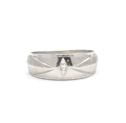 Close straight-on view of the wide band's face filling the frame, the single-cut diamond glinting in its pointed-oval recess at the centre of the engraved star, brushed white gold either side.