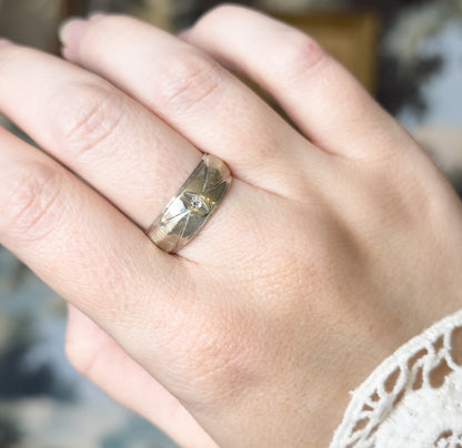 Mid-Century wide band ring in 14K white gold, shown on a finger, its broad textured face centred with a small single-cut diamond and tapering toward the narrower shank.
