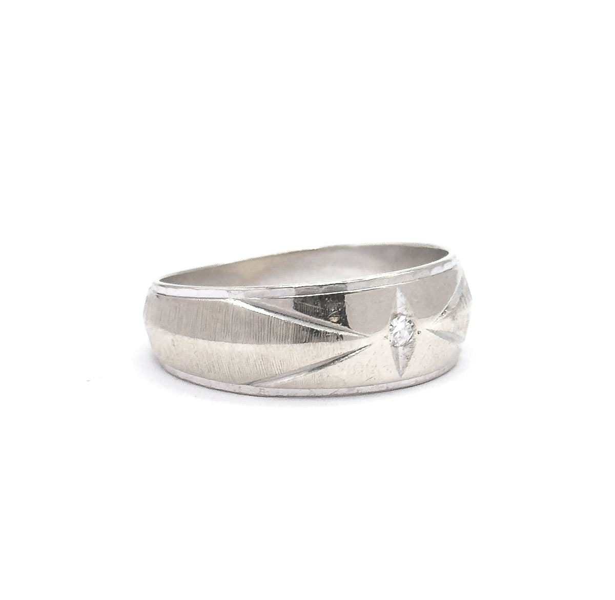 Shown off the hand upright against a plain white background, the broad face lit so its star-like engraved lines radiate from the small single-cut diamond toward the tapering shank.