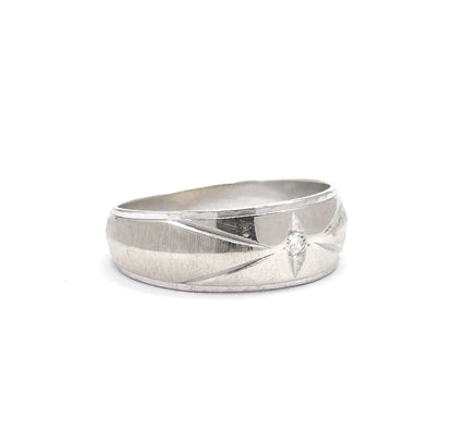 Shown off the hand upright against a plain white background, the broad face lit so its star-like engraved lines radiate from the small single-cut diamond toward the tapering shank.