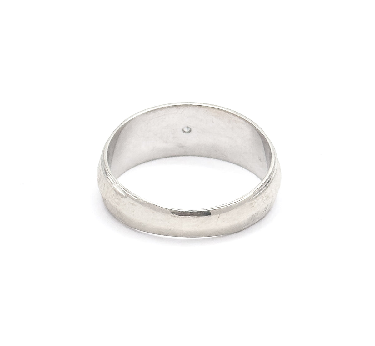 Tilted to show the plain underside of the band from behind, the smooth outer surface uninterrupted here while the small point of the diamond is just visible inside the hoop.