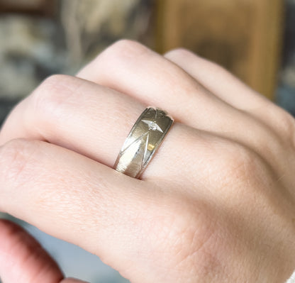 Shown on a finger of a hand held against a blurred background, the wide white gold face angled toward the camera so the band's scale across the knuckle is clear.
