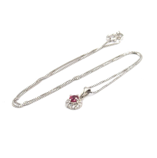 The whole necklace laid flat on white, showing the box-link sterling silver chain looped round to its spring-ring clasp, with the ruby and diamond halo pendant on its bail at the lower centre.