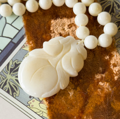 Close-up on the carved gourd pendant, its lobed fruit and leaf detail filling the frame, with the knotted cord passing through the top and beads receding to the upper right.