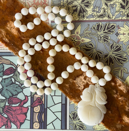 Overhead view of the whole strand coiled in an S-curve across the velvet band and two printed floral pages, knots visible between the jade beads and the carved gourd pendant at lower right.