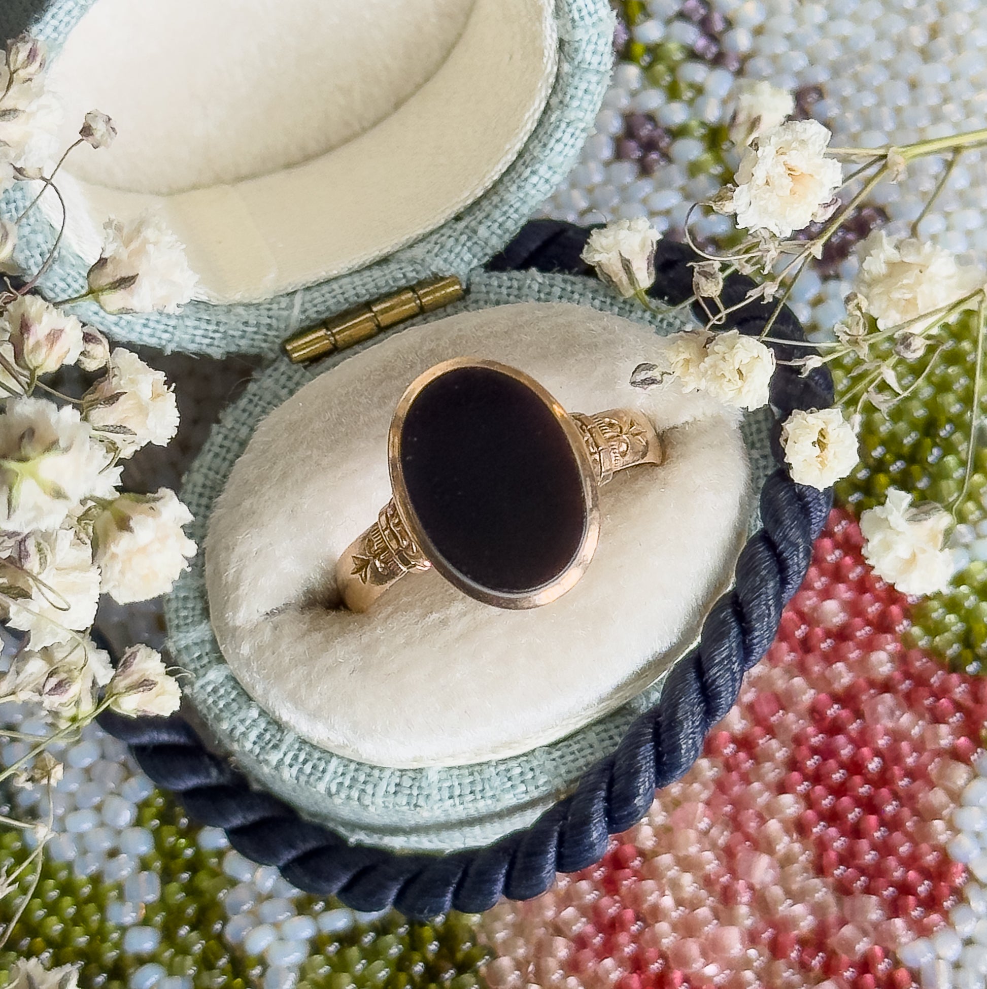 Now resting face-up in a pale open ring box among dried white flowers, the oval black agate filling its smooth bezel with engraved shoulders curving away on each side.