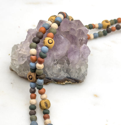 Strands draped over a chunky pale purple rock on white, with the beads trailing down in front of it and two of the larger marked ochre beads facing the camera.