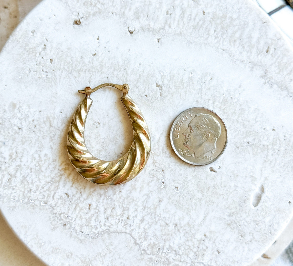 A single hoop lying flat on pale speckled stone next to a dime for scale, the oval standing about twice the coin's height with its hinged catch wire closed at the top.